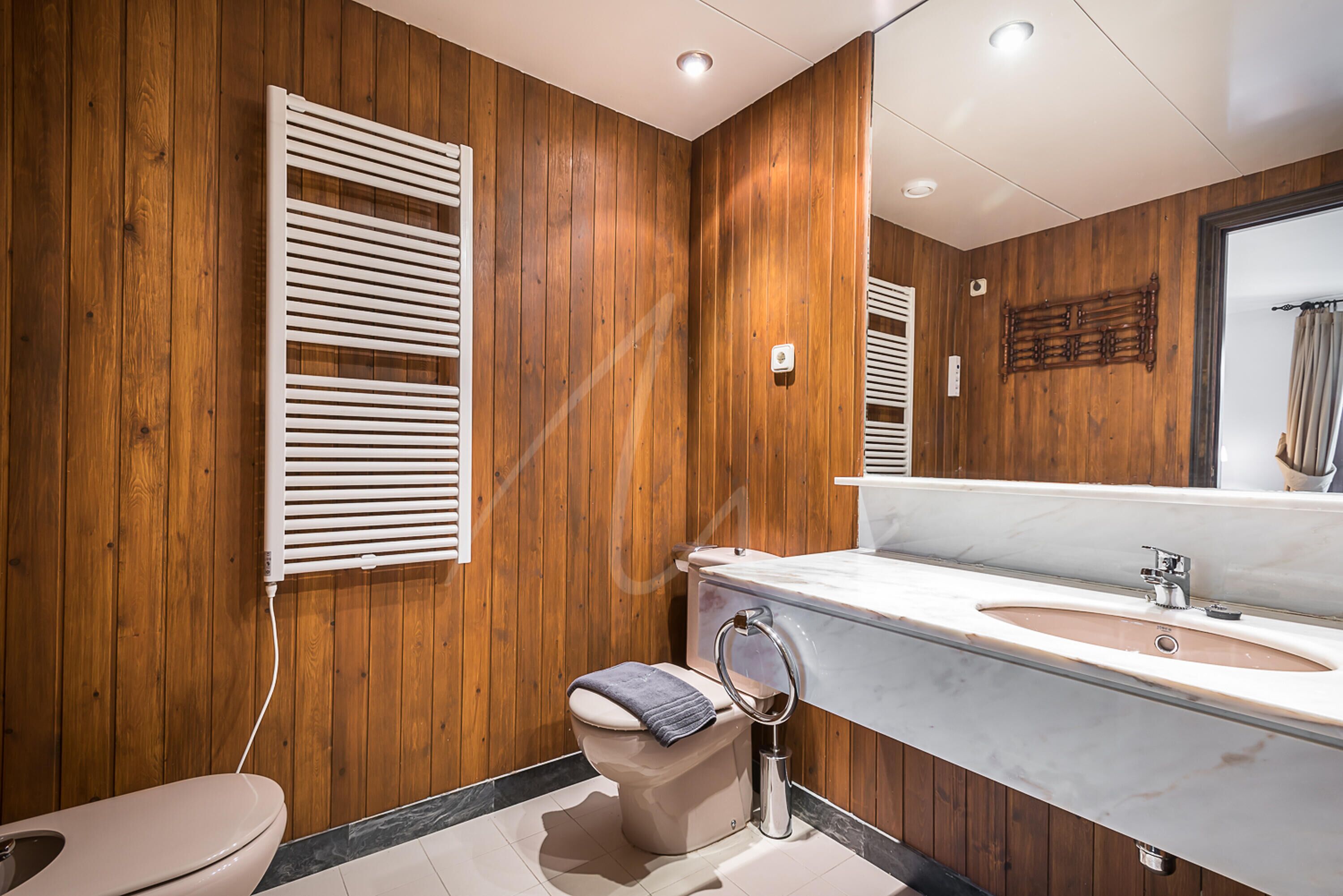 A modern bathroom with wooden panel walls, a toilet, a sink with a mirror, and a towel rack.