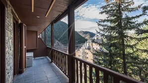Un balcon doté d’un mur en pierre, d’une balustrade en bois et offrant une vue sur un paysage montagneux.