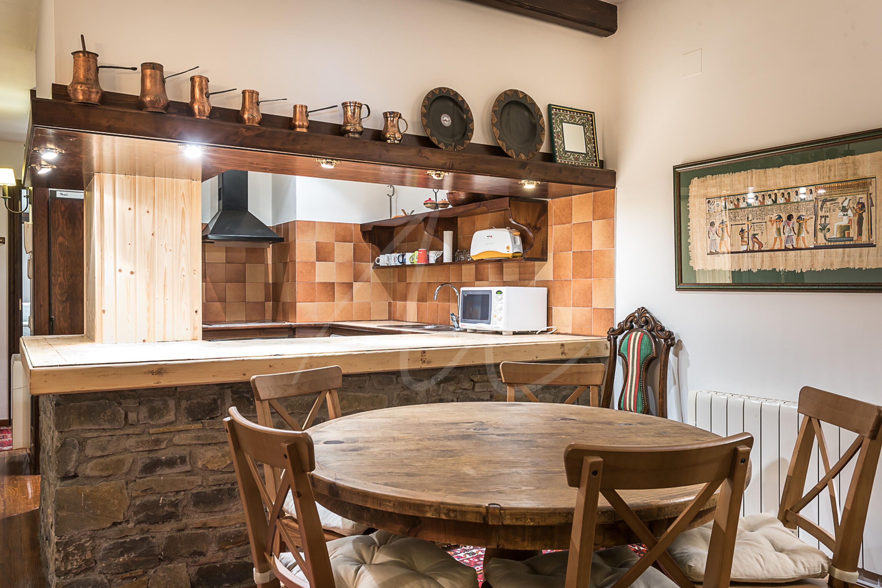 A kitchen with a wooden island, stone wall, and copper pots on the shelf.
