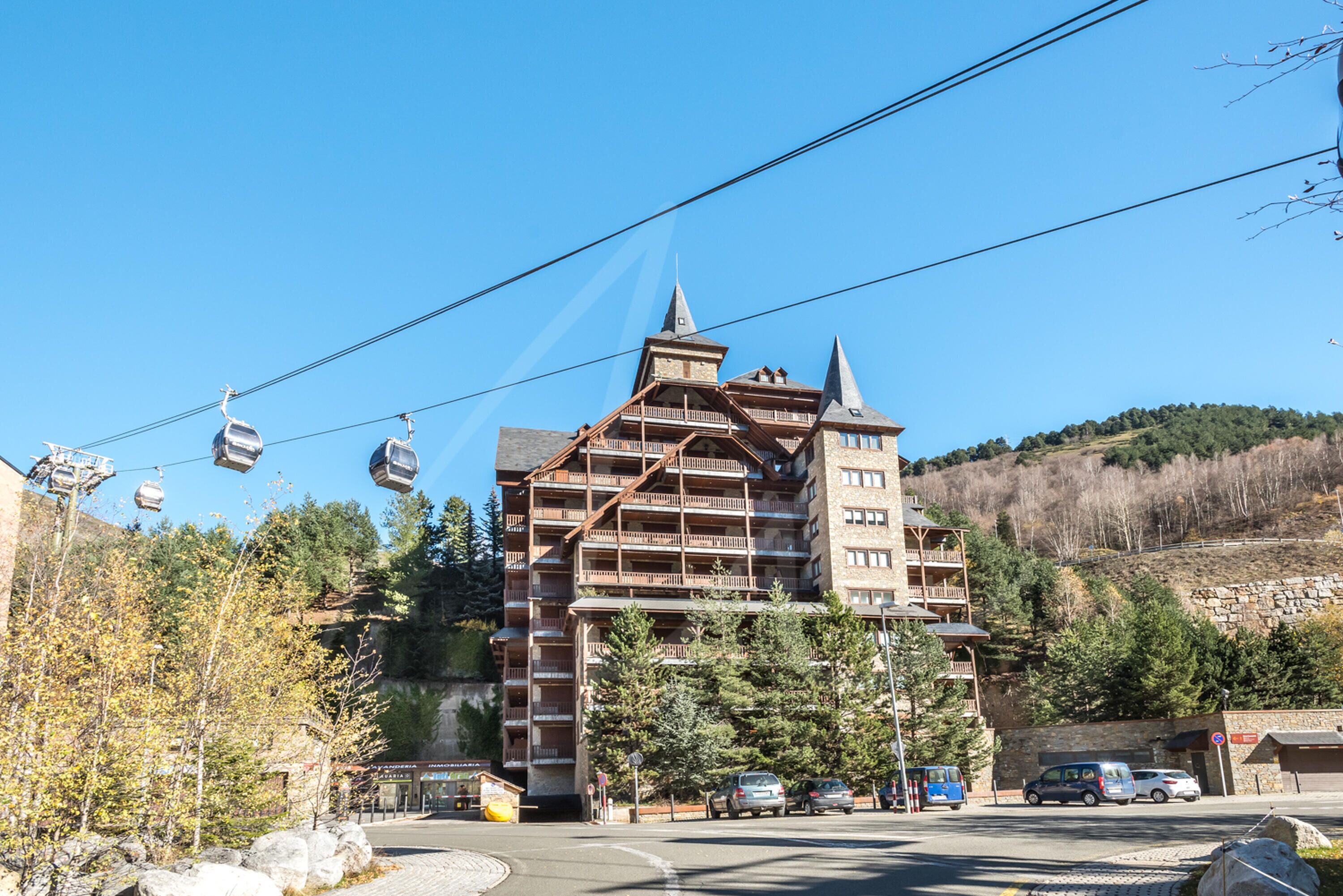 Un edificio a più piani con facciata in legno, balconi e una seggiovia sullo sfondo.