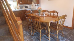 A dining area with a wooden table and chairs, a microwave, and a clock on the wall. - Dairy Cottage East Challoch Farm (Stranraer)