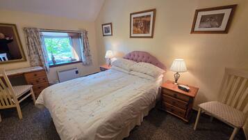A bedroom with a bed, two bedside tables, a chair, a dresser, a window with curtains, and wall-mounted pictures.