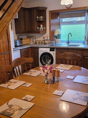 A kitchen with wooden cabinets, a washing machine, and a dining area with a table set for four. - Dairy Cottage East Challoch Farm (Stranraer)