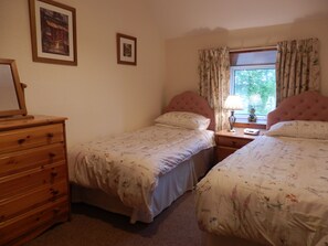 A bedroom with two single beds, a wooden dresser, a window with curtains, and framed pictures on the wall. - Dairy Cottage East Challoch Farm (Stranraer)