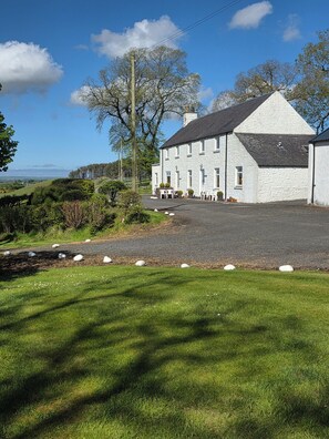 A white building with a grey roof, surrounded by a gravel driveway and a grassy area. - Dairy Cottage East Challoch Farm (Stranraer)