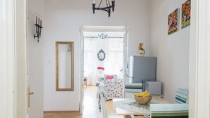En hall som leder till en matplats med ett fiskbensmönstrat golv, en kristallkrona, en spegel och en tv som står på ett skåp.