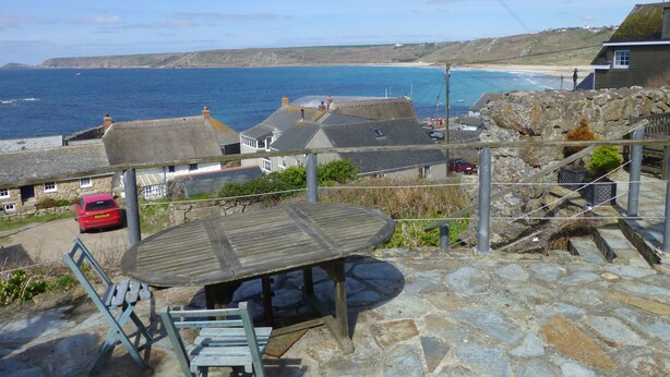 A coastal view with stone buildings, a wooden bench, and a red car.
