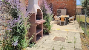 A brick building with a stone oven, a table with chairs, and purple flowering plants. - Big panoramic house in the Lucca hills. Pool, garden, WiFi, Aircon (Capannori)
