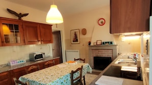 A kitchen with wooden cabinets, a dining table with chairs, a microwave, a sink, and a fireplace. - Big panoramic house in the Lucca hills. Pool, garden, WiFi, Aircon (Capannori)