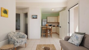 A living room with a sofa, a coffee table, and a patterned armchair. There is a kitchen in the background with wooden cabinets and a dining area.