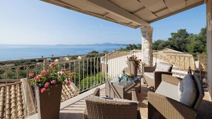 A balcony with wicker furniture, a potted plant, and a view of the sea.