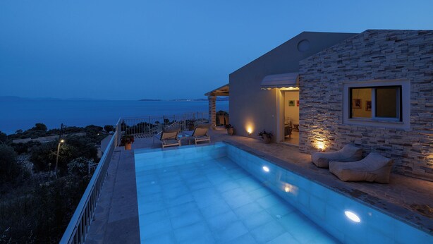 A modern house with a swimming pool, stone exterior, and a view of the sea.