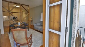 Un espacio de sala acogedor con un sofá de marco de madera, una silla de ratán y una mesa de comedor. Se ve una cocina con armarios de madera y un horno empotrado al fondo.