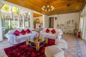 A living room with a glass coffee table, two sofas with red cushions, a red rug, and a wooden ceiling.