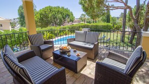 A covered outdoor seating area with wicker furniture, a pool, and a view of a residential neighborhood. - Villa Lira | 6 bedrooms | Spacious | Quinta do Lago (Quinta do Lago)