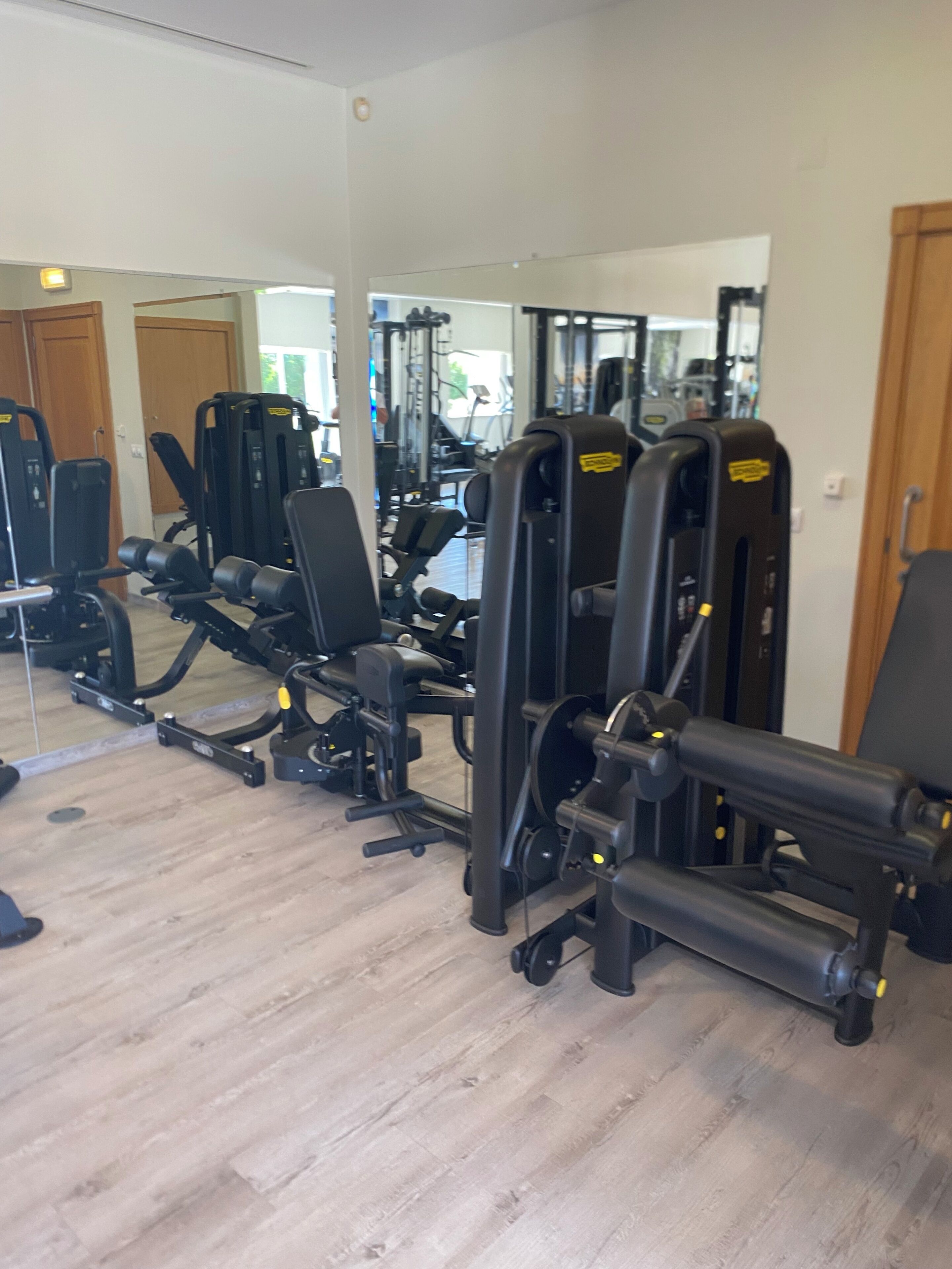 Une salle de sport équipée de divers appareils d’exercice, dotée d’un plancher en bois et de miroirs sur les murs.