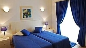 Quarto de hotel com duas camas, uma mesa de cabeceira com abajur e um quadro na parede.
