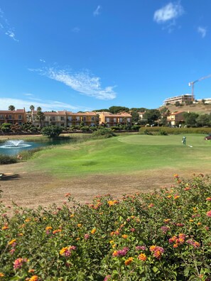 A golf course with a pond, a row of buildings, and a construction crane in the background.