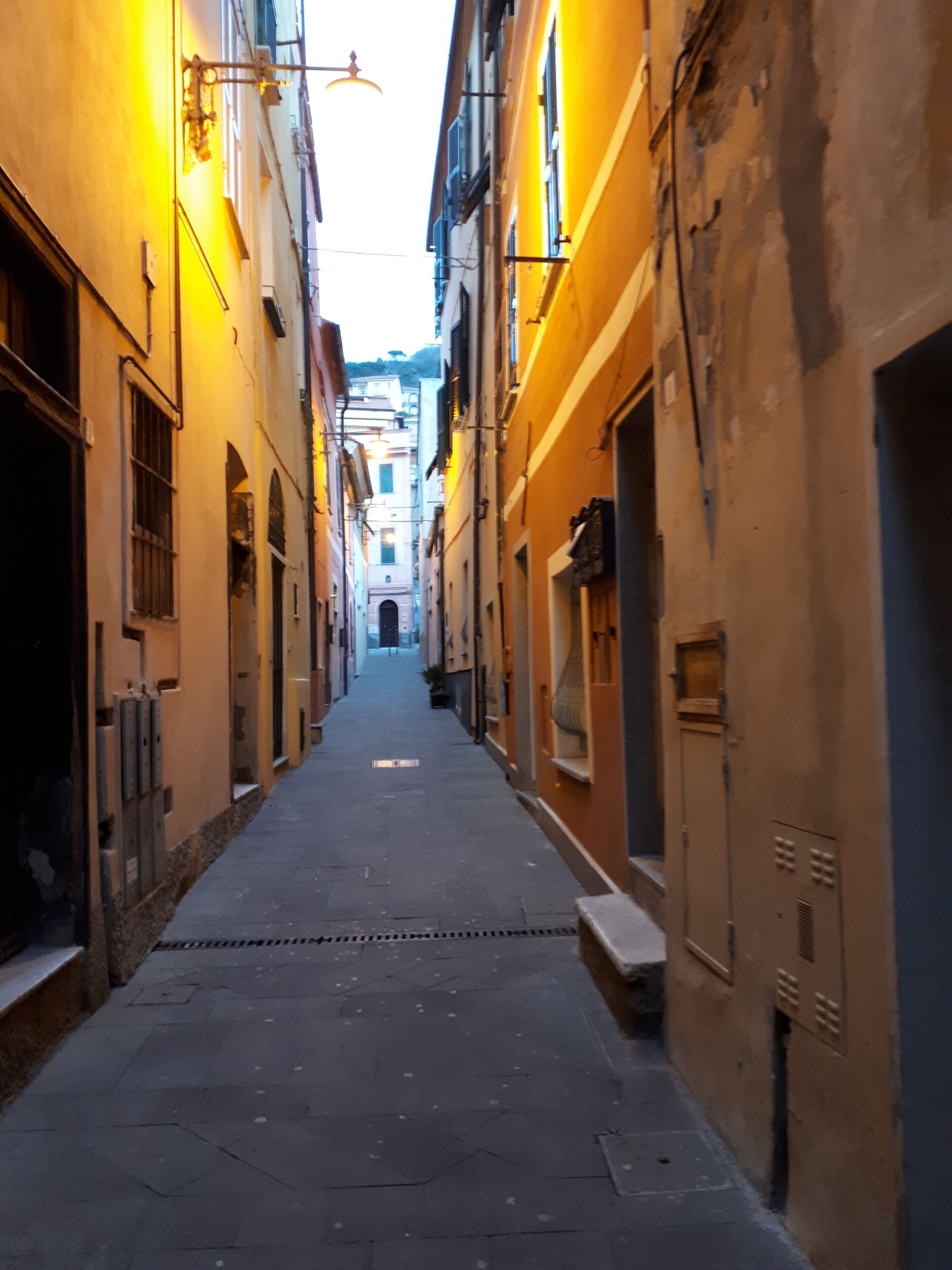 A narrow street flanked by buildings with visible windows and doors, suggesting a residential or mixed-use area.