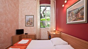 Ein Hotelzimmer mit Bett, Schreibtisch, Fernseher und Fenster mit Blick auf Grünflächen.