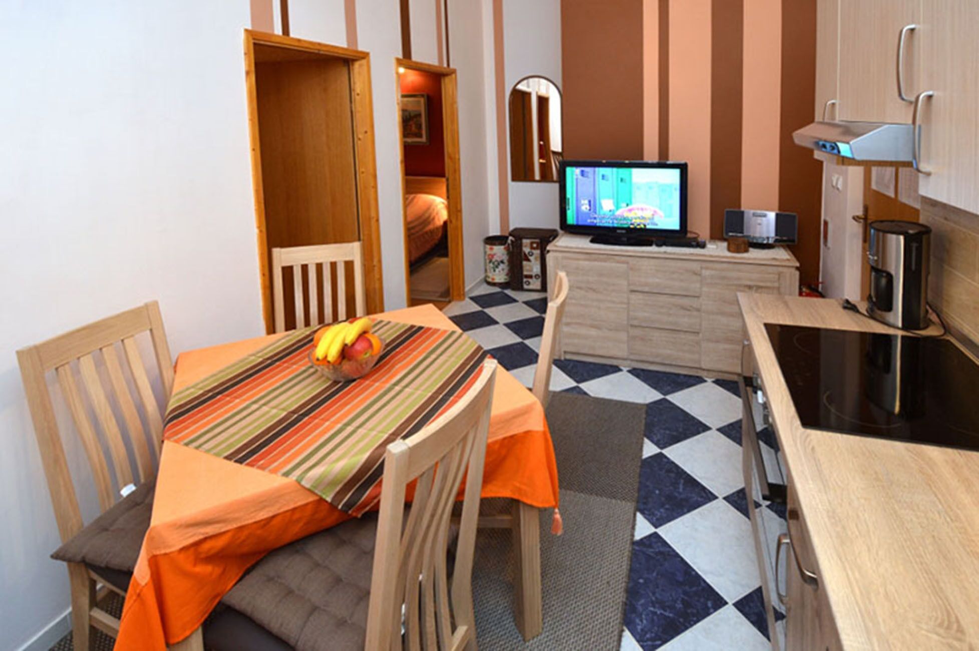 Una habitación compacta con mesa de comedor, sillas, televisor, cafetera y kitchenette.