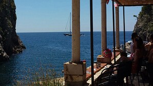 Eine Seeterrasse mit Säulen aus Stein, Blick auf das Meer und ein Schiff in der Ferne.