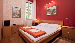 Ein Schlafzimmer mit einem Bett, Nachttischen, einem Schreibtisch, einem Stuhl und zwei gerahmten Bildern an der Wand.