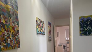 A hallway with white walls, tiled floor, and artwork. There is a door leading to a kitchen area with appliances. - Casa al Mare, Villa Bella (Augusta)