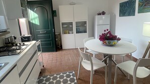 A compact kitchen with a gas stove, white cabinets, a dining table with chairs, and a patterned rug. - Casa al Mare, Villa Bella (Augusta)