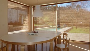 A dining area with a round table and chairs, large windows with blinds, and a hanging light fixture. - Large Holiday House in the Alto Minho- Vila nova de Cerveira - Max. 17 people (Vila Nova de Cerveira)