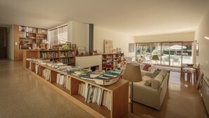 A spacious living area with a large bookshelf, a cozy sofa, and a view of a swimming pool through large windows. - Large Holiday House in the Alto Minho- Vila nova de Cerveira - Max. 17 people (Vila Nova de Cerveira)