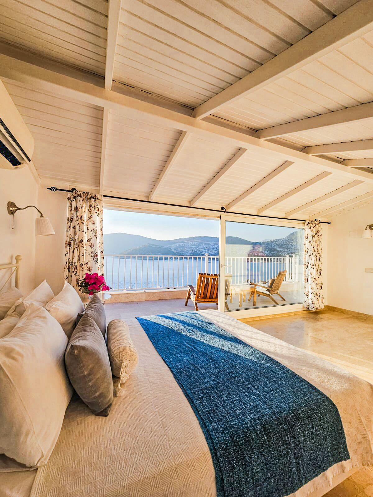 A bedroom with a large bed, a view of the sea, and a balcony with a chair.