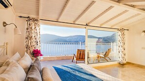 Une chambre avec un grand lit, une vue sur la mer et un balcon équipé d’une chaise.