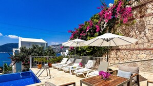 Un espace aménagé au bord de la piscine, avec des chaises longues, une table et des parasols.