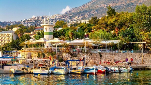 Un port de plaisance situé sur la côte, avec des bateaux amarrés, un phare et un mur de pierre sur lequel se trouve un restaurant offrant une vue sur l’eau.