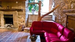 A stone fireplace, a red leather sofa, and a wooden table with a vase of flowers in a rustic room.