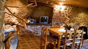 A rustic stone-walled room with a wooden dining table and chairs, a television, and a fireplace.