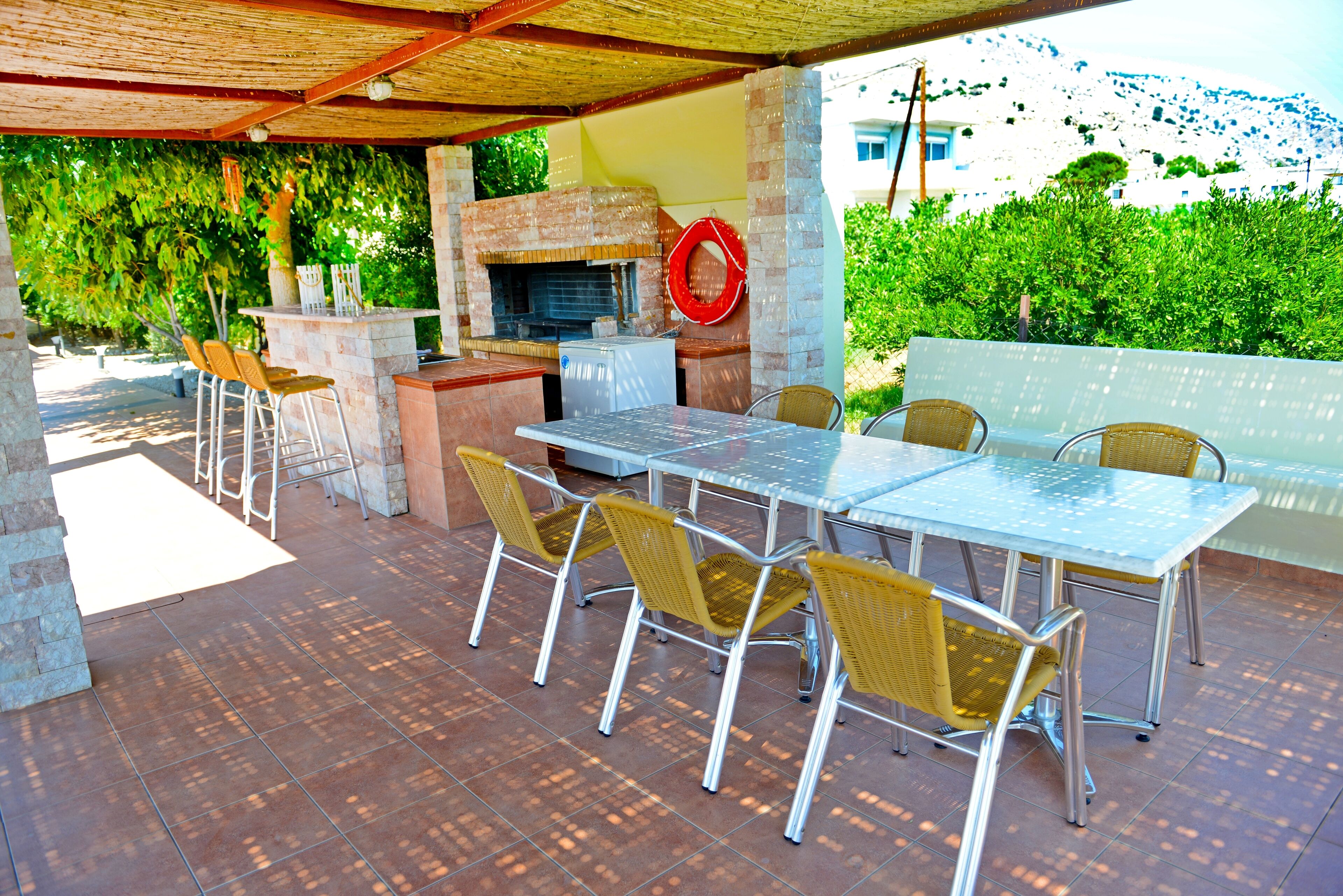 An outdoor patio with a brick barbecue, metal table, wicker chairs, and a glass railing.