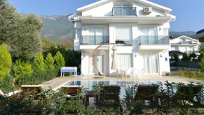 Una casa moderna de dos pisos con piscina, mobiliario exterior y telón de fondo de montañas.