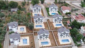 Un conjunto residencial con varias casas de dos pisos, cada una con piscina y patio cercado.