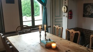 A dining area with a wooden table, chairs, a candle, and a window with curtains. - Lovely Former Bakery In The Seven Valleys (Embry)