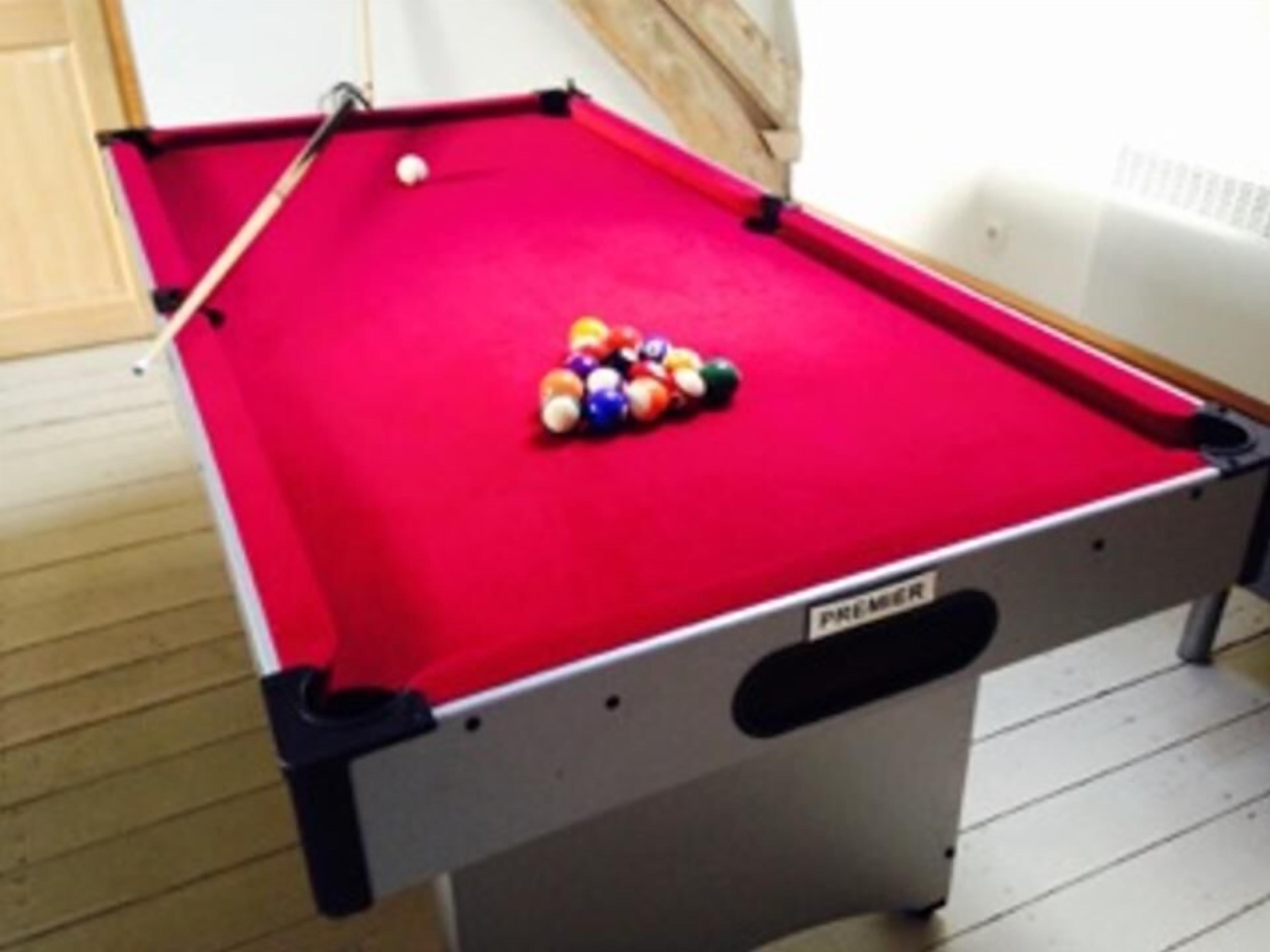 A pool table with a red felt surface and a cue stick.