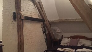 A bedroom with a sloped ceiling, a wooden bed frame, a nightstand, and a brick wall. - Lovely Former Bakery In The Seven Valleys (Embry)