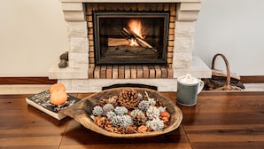 A fireplace with a fire, a bowl of pinecones, and a mug on a wooden table. - Secluded Sunset Villa on Cliff & 180° Ocean Views (Calheta)