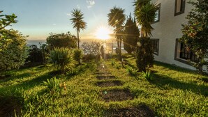 A garden pathway leading to a building with a view of the ocean at sunset. - Secluded Sunset Villa on Cliff & 180° Ocean Views (Calheta)