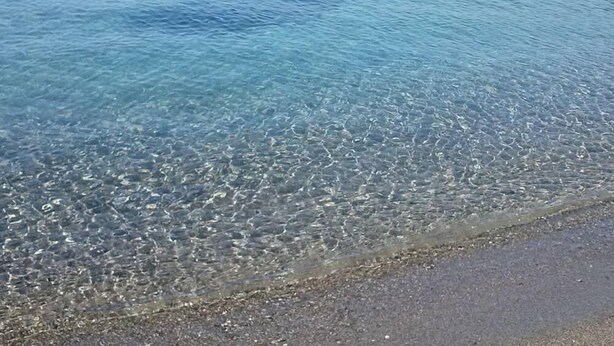 A clear view of a beach with shallow water revealing pebbles and sand at the shore.