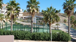 A tennis court surrounded by palm trees and a modern building with a curved roof. - Beautiful apartment with private pool, wifi, tv, close to all amenities (Orihuela Costa)