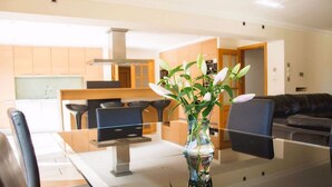 A modern kitchen with wooden cabinets, a stainless steel range hood, and a dining area with a glass table and chairs.