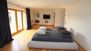 A modern bedroom with a large bed, a television, and a sliding glass door to a balcony.