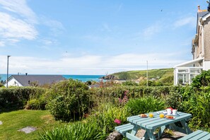 A garden with a table set for breakfast, overlooking a coastal view.
